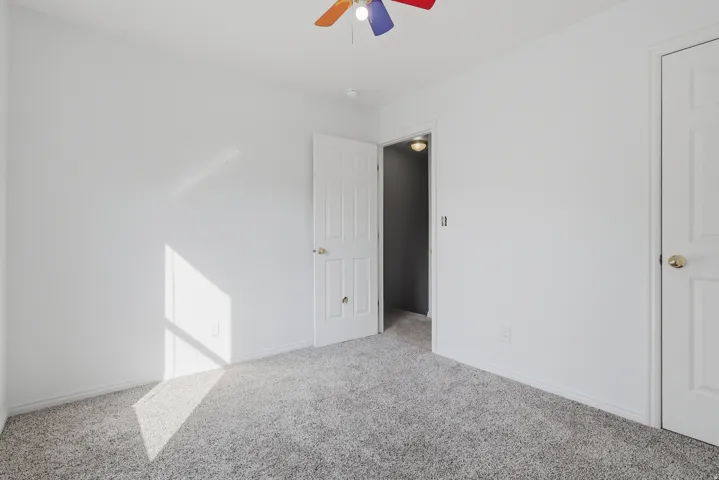 Neutral tone wall finish, textured carpet flooring, white paneled doors, and a ceiling fan
