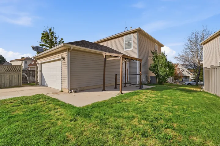 Detached garage with automatic door, concrete driveway, pergola-covered patio, and a manicured lawn