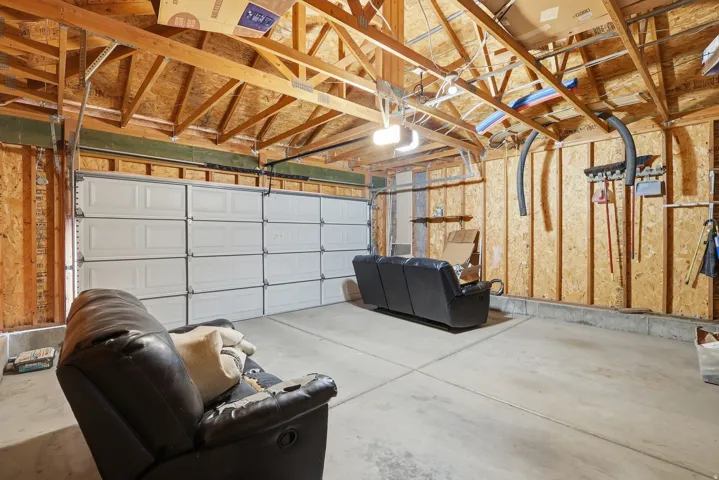 Spacious garage featuring exposed wood framing, concrete flooring, and a multiple-panel garage door