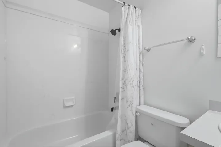 White bathtub and shower combination with a black shower head, and a white toilet