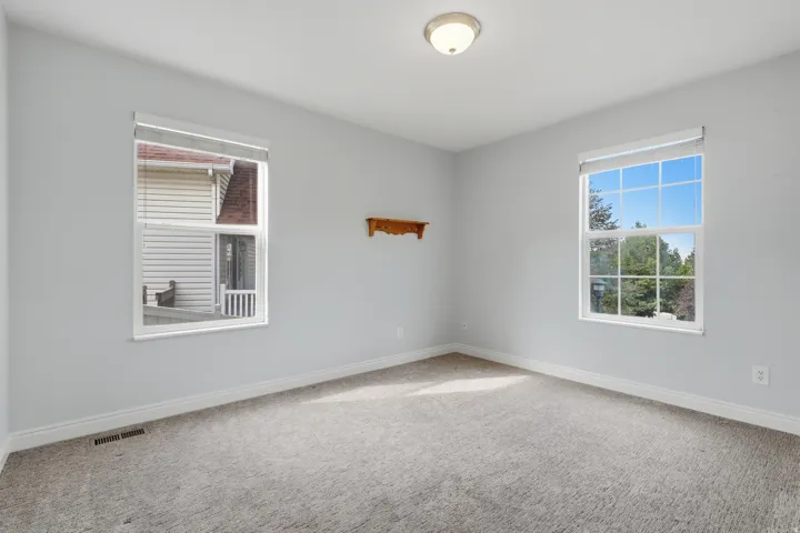 Bright corner bedroom with dual windows flooding the space with natural light, neutral carpeting, and fresh white walls