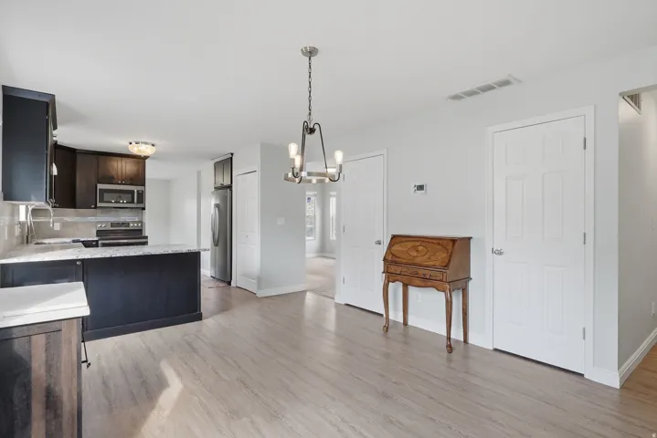 Open-concept kitchen and dining area featuring wood-finish flooring throughout, dark cabinetry with stainless steel appliances, pendant lighting, and white six-panel interior doors