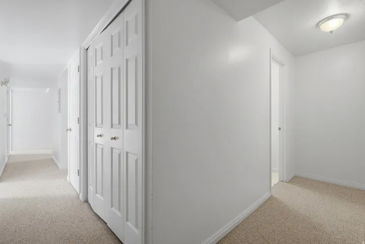 Hallway featuring light-toned carpeting, white walls, and a bi-fold closet door