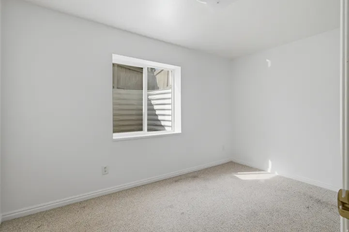Bright, neutral bedroom showcasing neutral carpet flooring, clean white walls, and a casement window with horizontal blinds providing natural light