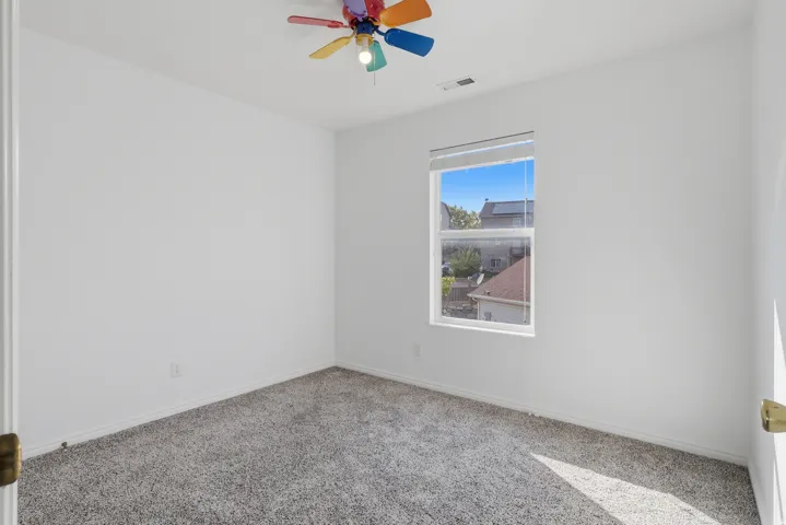Bright secondary bedroom featuring neutral carpeting, large double-hung window with natural light, and a colorful ceiling fan with integrated lighting fixture