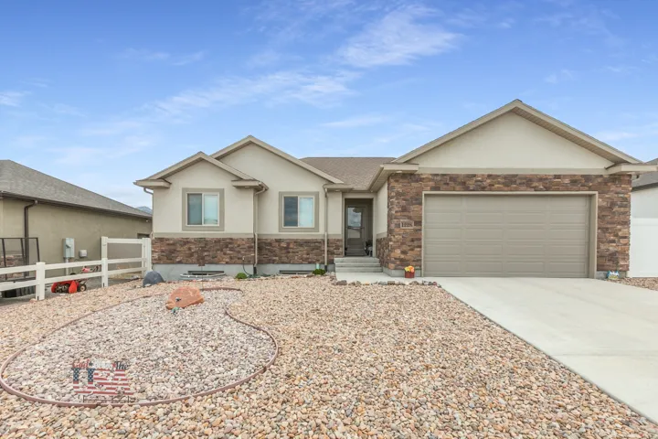 Single-story residence featuring a two-car garage, stone and stucco exterior, and a rock landscaping design