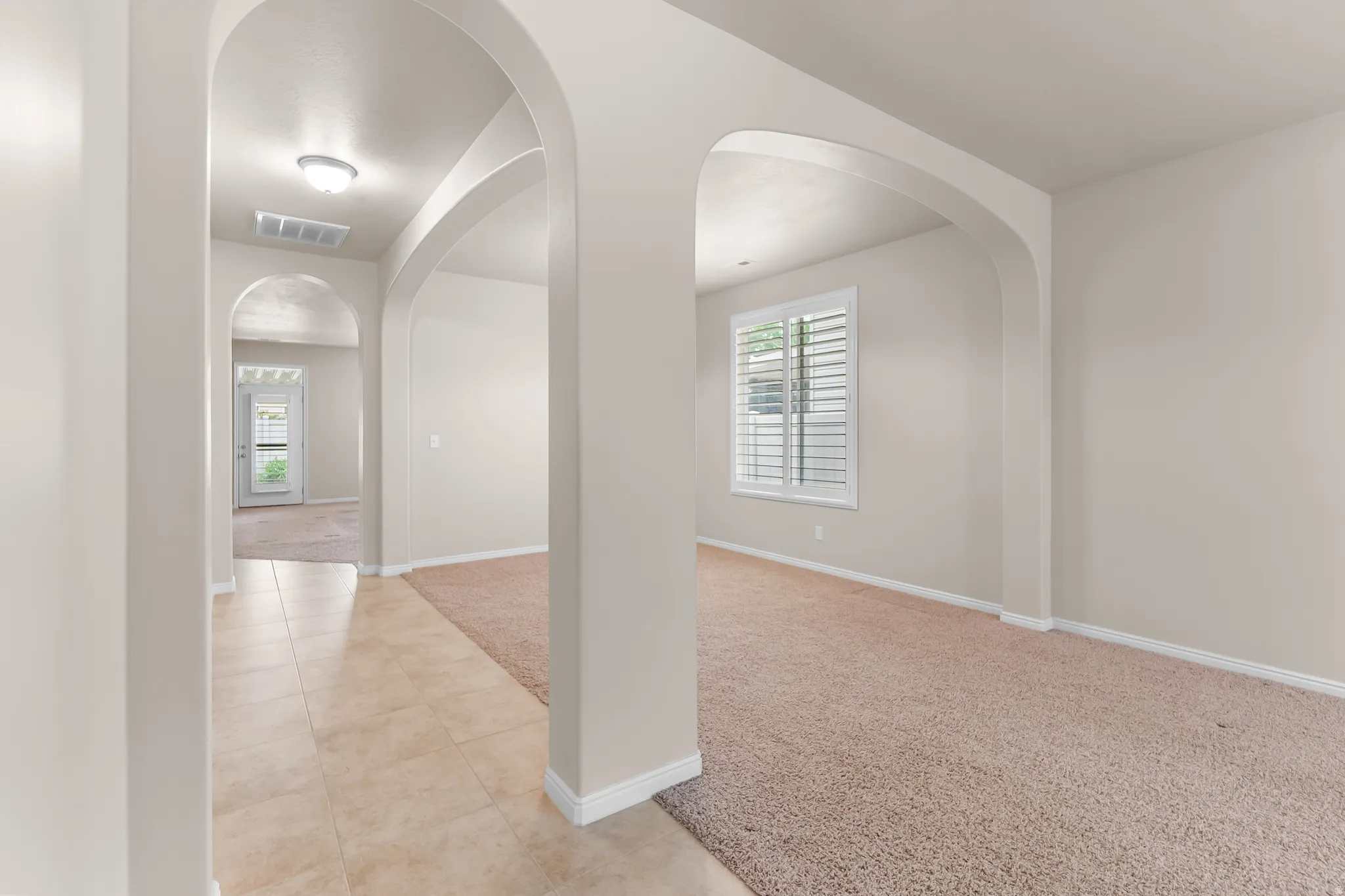 Archways defining interior spaces, light-colored walls, and a window with plantation shutters
