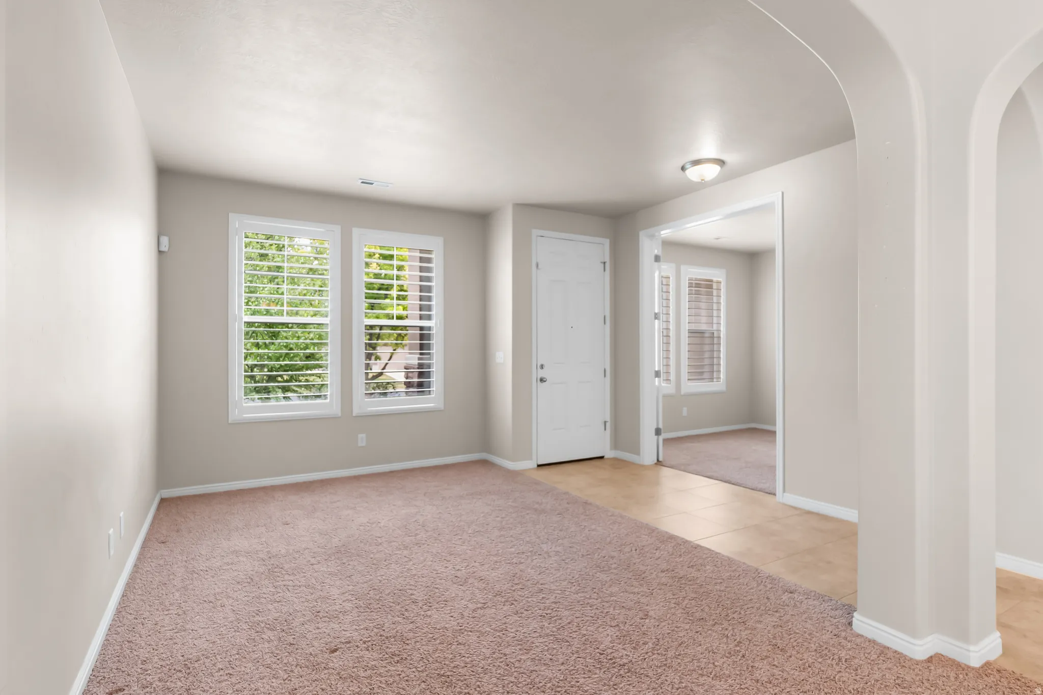 Room featuring neutral wall tones, plush carpeting, two windows with plantation shutters, a white paneled door, and a light fixture