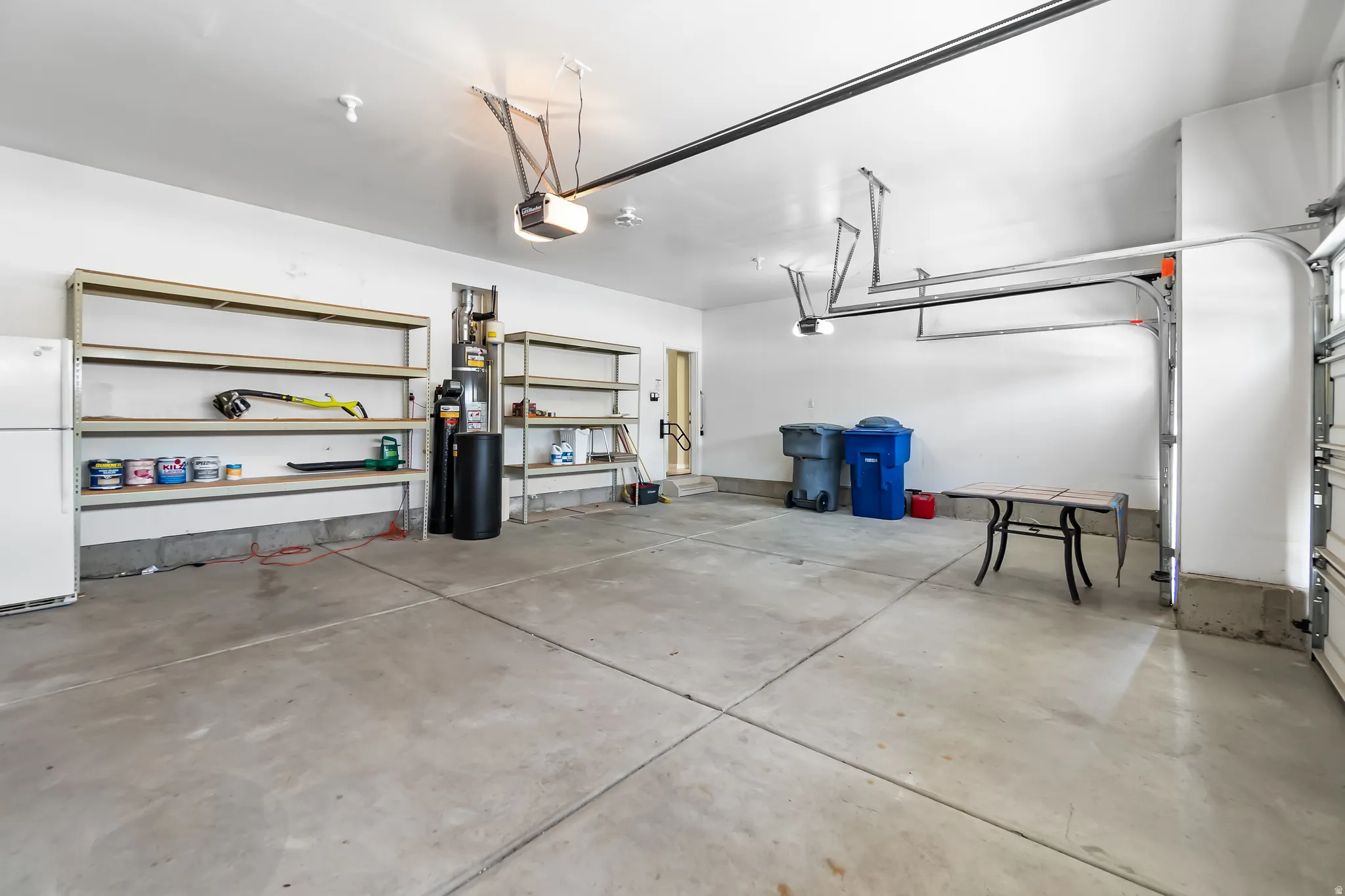 Spacious garage featuring a concrete floor, high ceilings, multiple built-in shelving units, and two overhead garage door openers