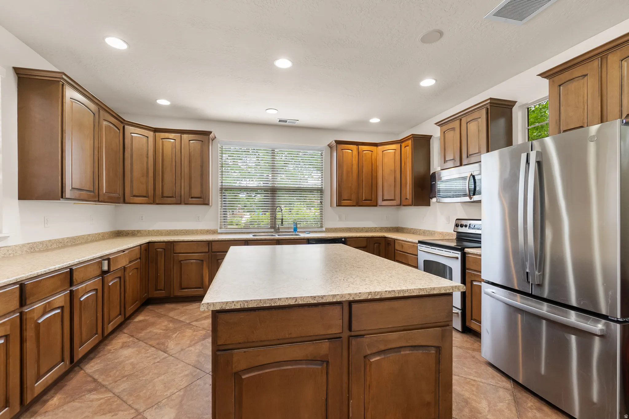 Kitchen featuring wood cabinetry, stainless steel appliances, a center island, composite countertops, and recessed lighting