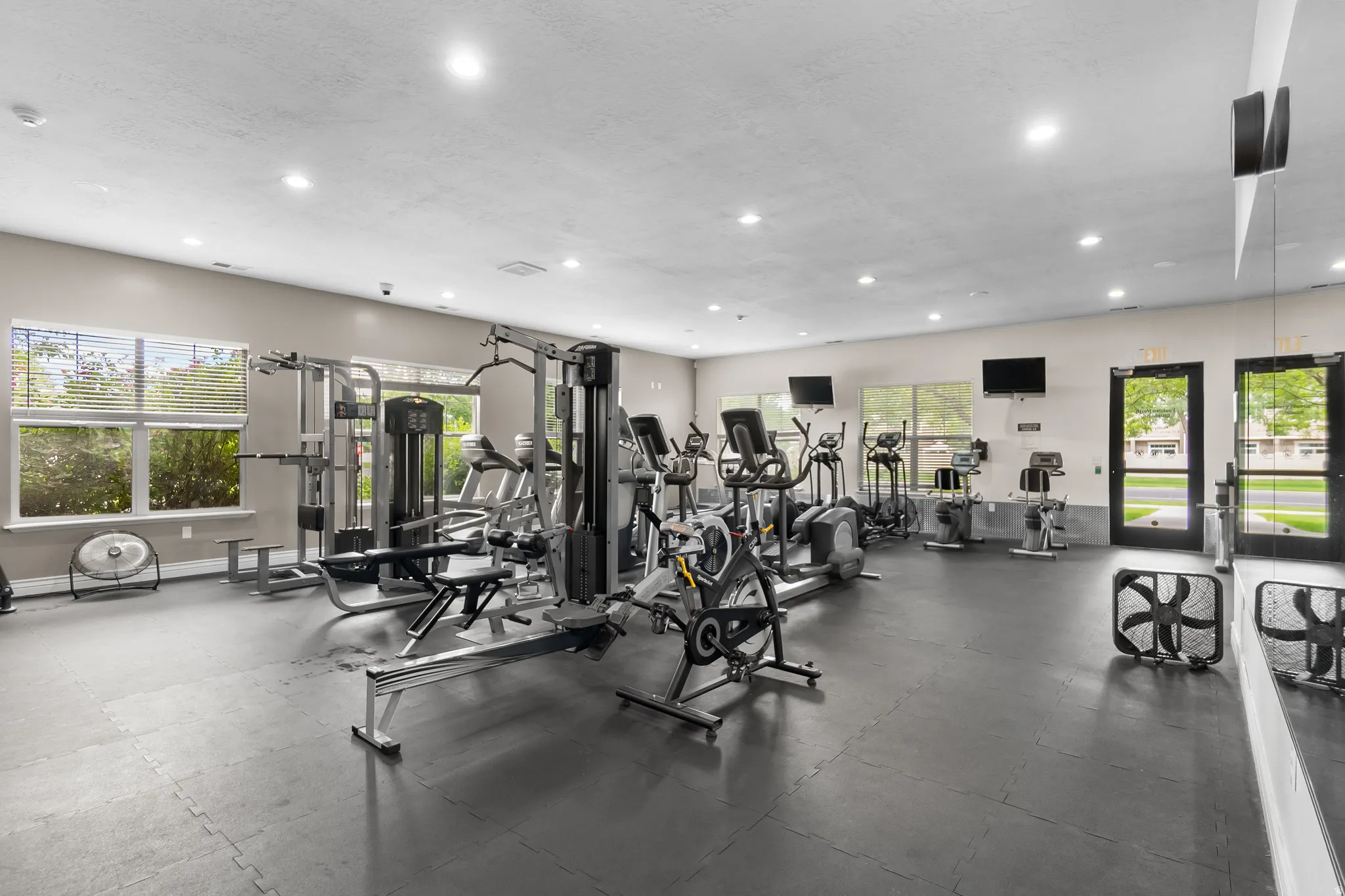 Fitness center featuring extensive exercise equipment, rubberized flooring, abundant natural light from multiple windows, recessed ceiling lighting, and wall-mounted televisions