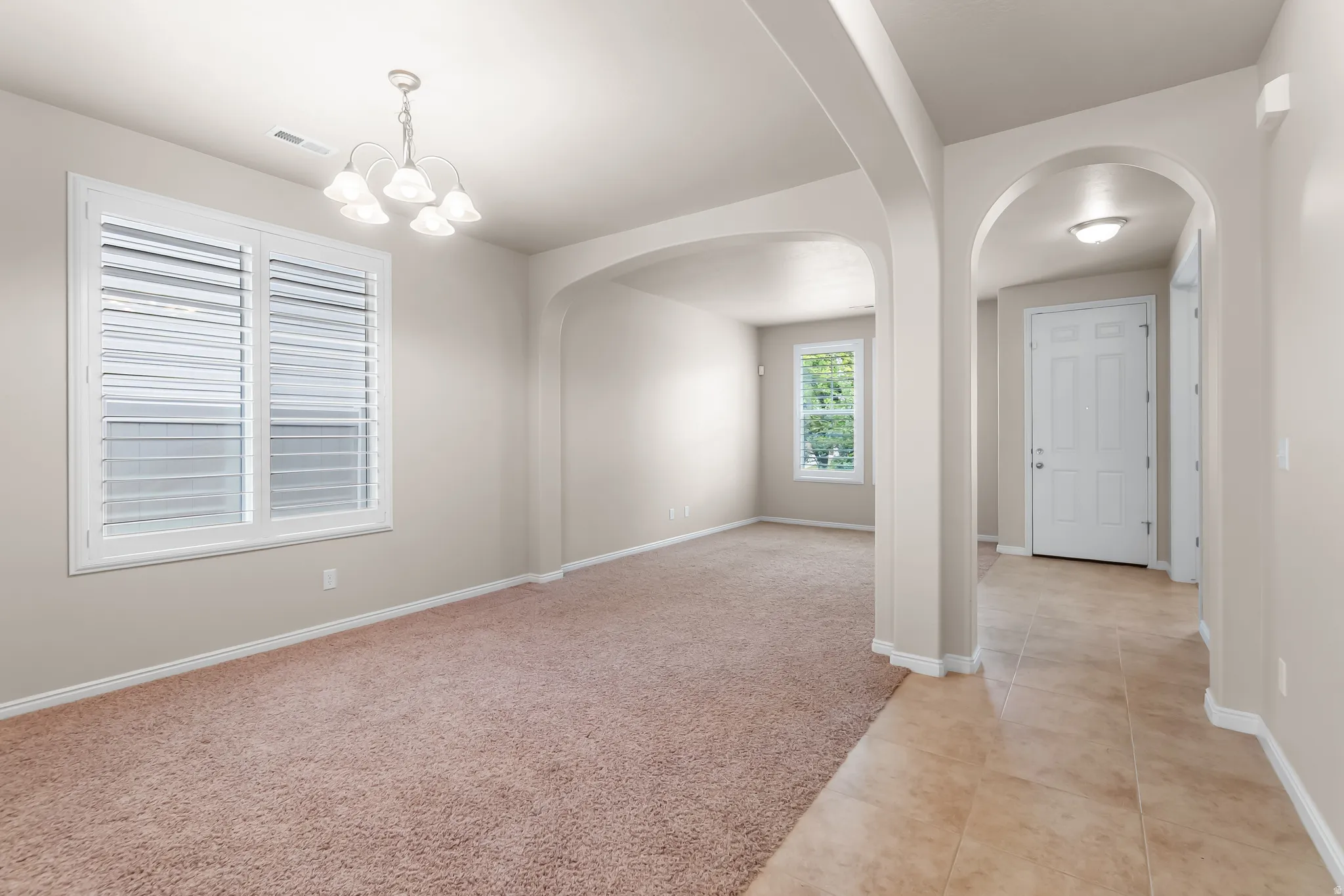 Spacious room featuring neutral carpeting, white plantation shutters, and a five-light chandelier