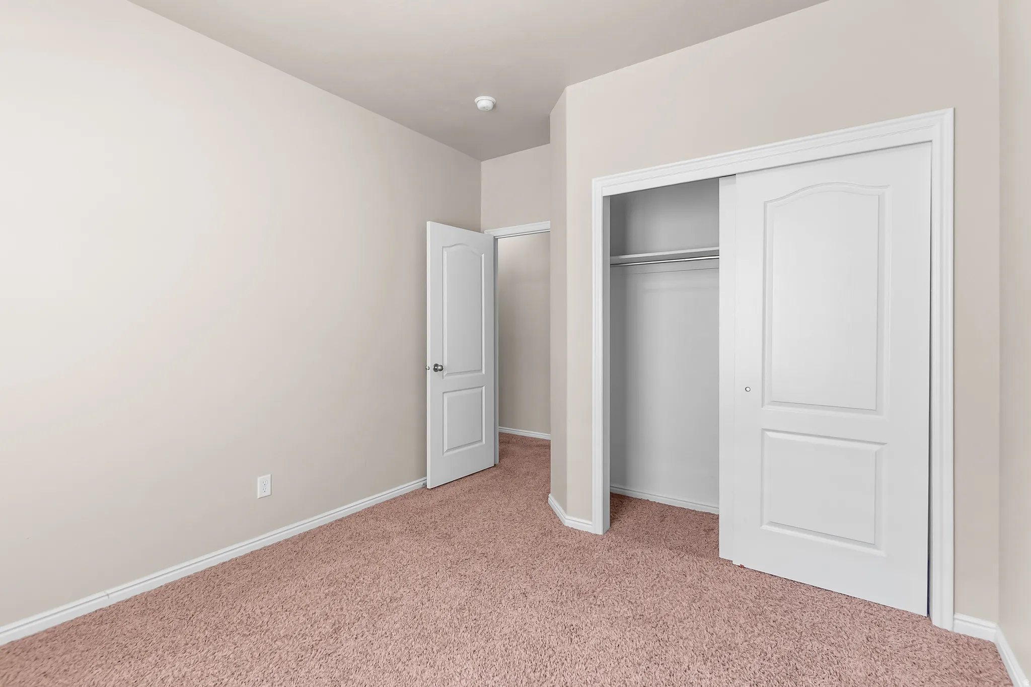 Room featuring neutral wall paint, light brown carpeting, a white interior door, and a closet with white sliding doors and an interior rod and shelf