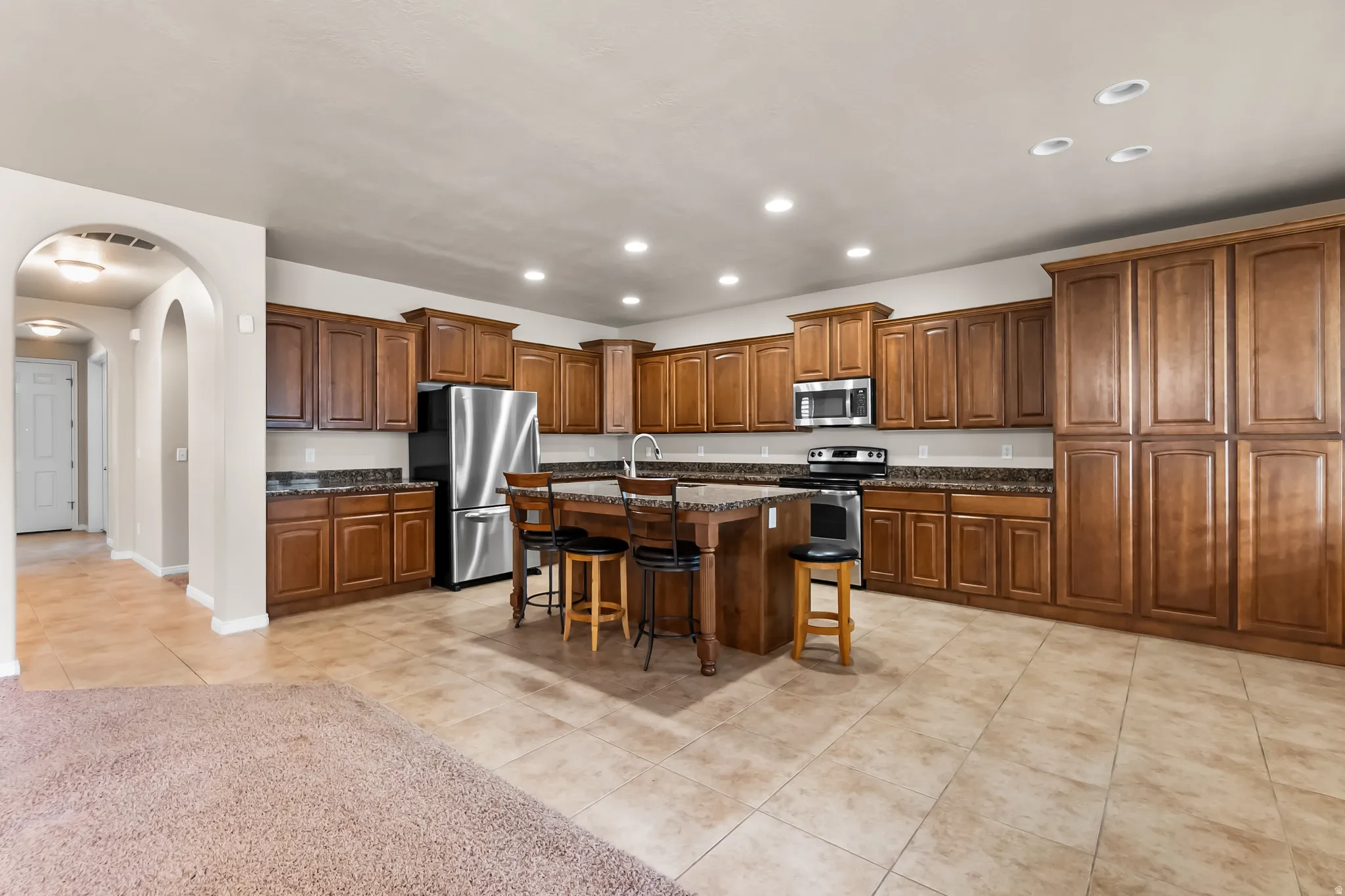 Kitchen featuring a substantial central island, extensive wood cabinetry, stainless steel appliances, recessed lighting, and tile flooring