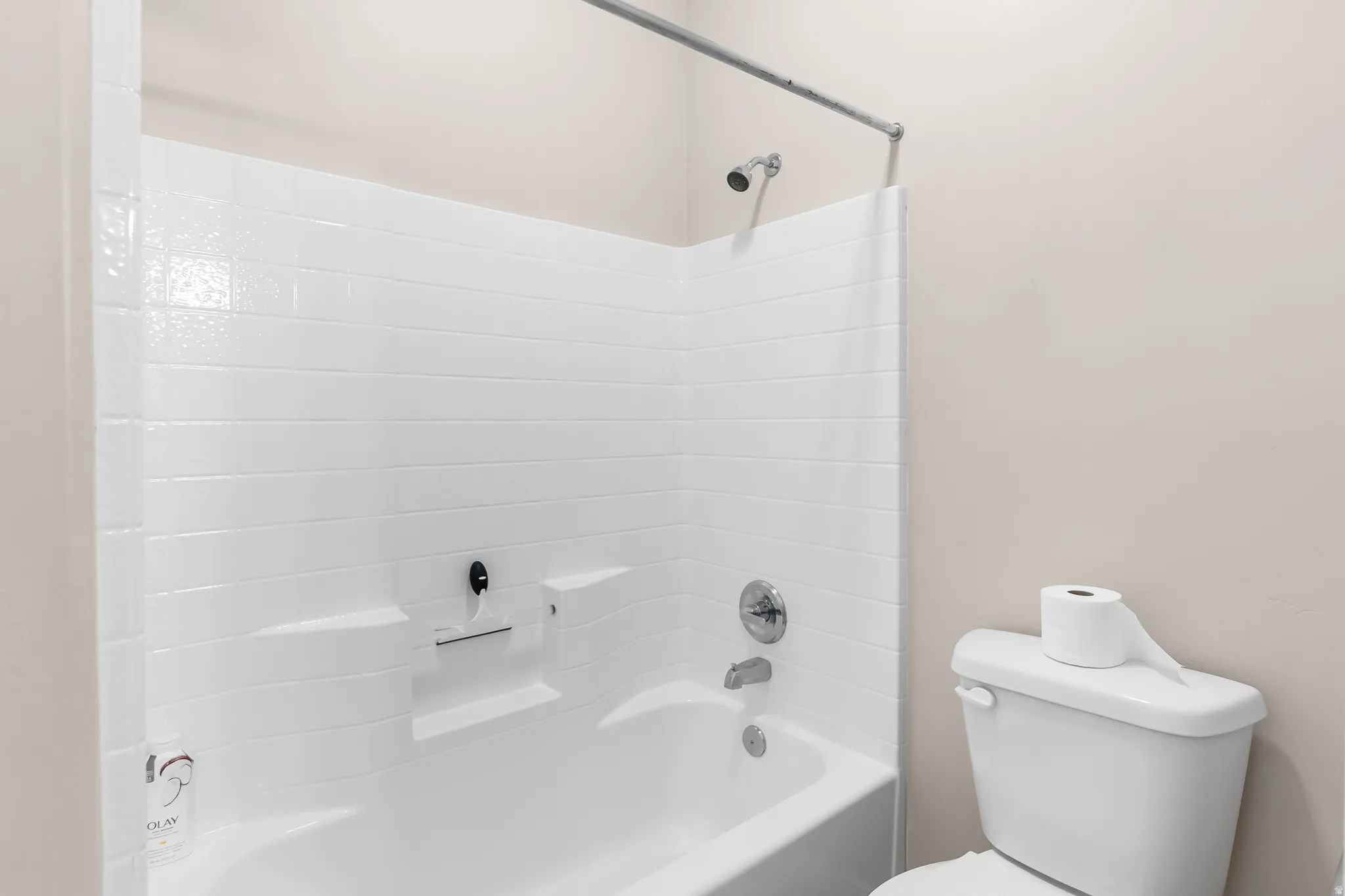 Tub and shower combination featuring white subway tile surround, chrome fixtures, and an integrated shelf