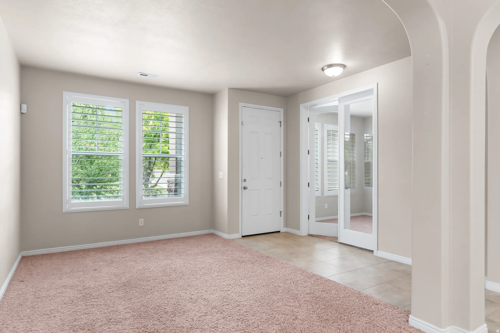 Entryway featuring light-toned walls, two framed windows with white louvered shutters, and a white entry door