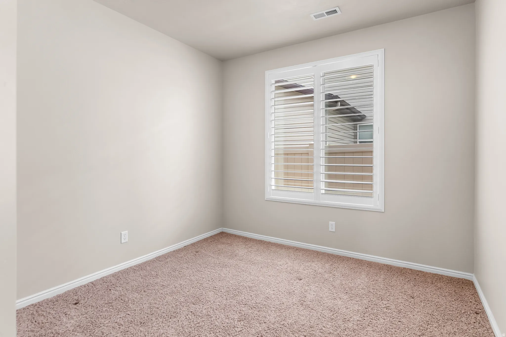 Room featuring neutral wall paint, white baseboards, plush carpet flooring, a window with white plantation shutters, and a ceiling vent