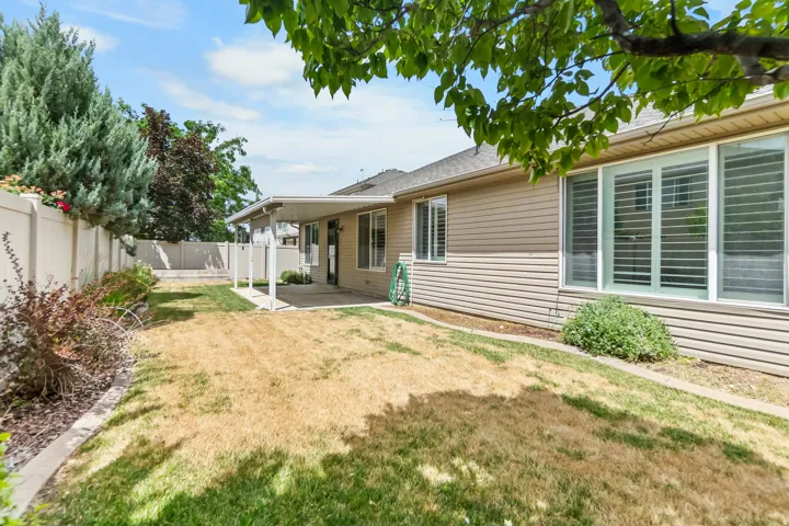 Expansive backyard featuring a covered patio, concrete hardscaping, vinyl fencing, mature landscaping, and bay windows with plantation shutters