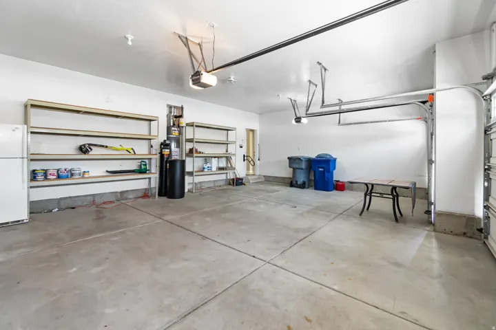 Spacious garage featuring a concrete floor, high ceilings, multiple built-in shelving units, and two overhead garage door openers