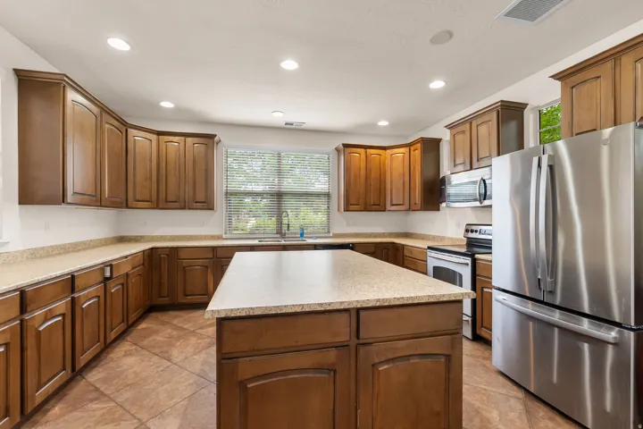 Kitchen featuring wood cabinetry, stainless steel appliances, a center island, composite countertops, and recessed lighting