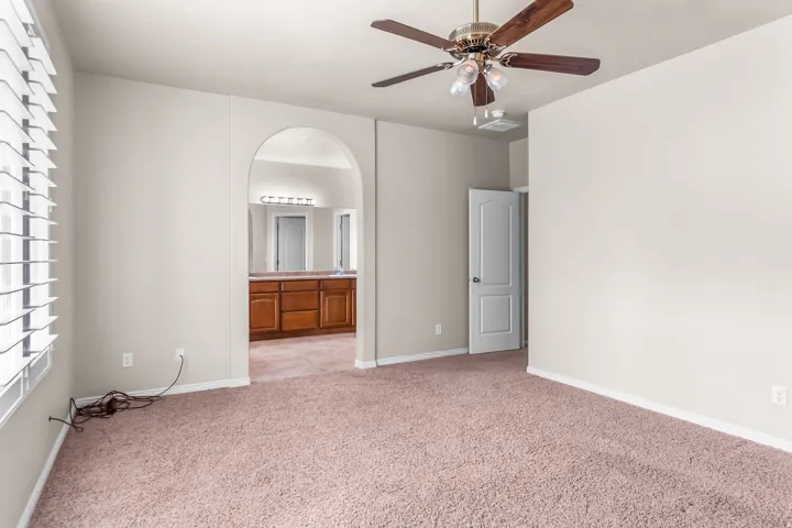 Spacious room featuring neutral paint, plush carpeting, a ceiling fan with light fixture, and arched entryway