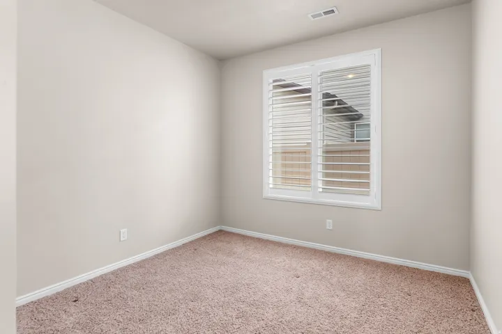 Room featuring neutral wall paint, white baseboards, plush carpet flooring, a window with white plantation shutters, and a ceiling vent