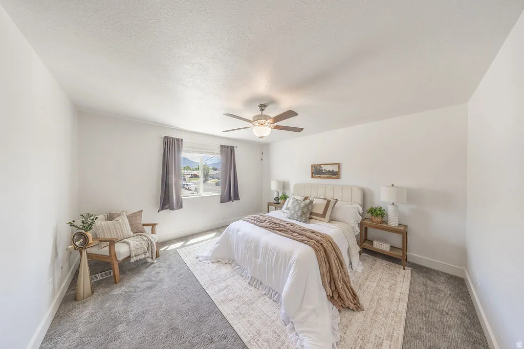 LARGE primary bedroom.  Neutral wall color, ceiling fan with light fixture, window with drapery, and carpeted flooring.