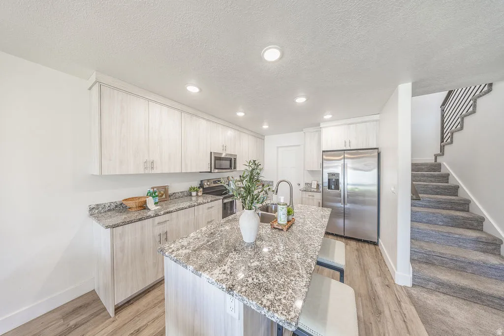 Modern kitchen featuring light wood-finish cabinetry, stainless steel appliances, granite-style countertops, an island with seating, and LVP flooring