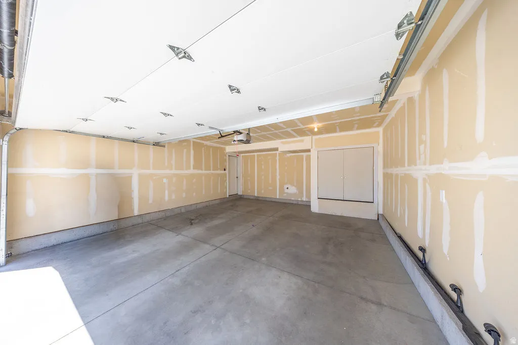 Spacious two-car garage featuring a concrete floor, an overhead door with an automatic opener, and a side access door.  App for garage door opener so you can control it from anywhere.