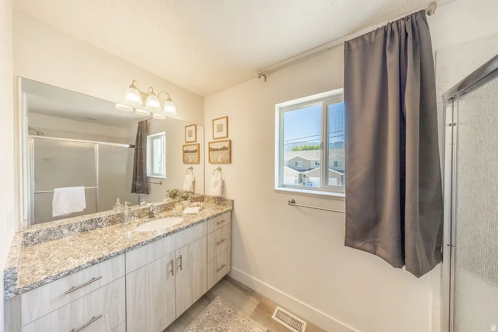 Granite countertop.  Large wall mirror.  Modern light fixture.  Sliding glass doors to shower viewable in mirror.