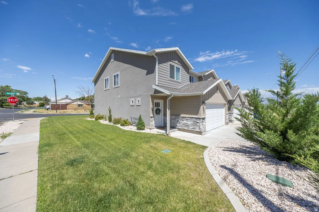 Multi-level property featuring a stucco and siding exterior, an attached garage, a manicured lawn, and a decorative stone landscaping bed!!!