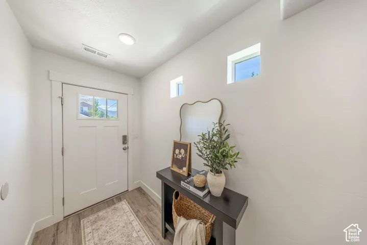 Entryway with a white paneled door featuring multiple glass lites, LVP flooring, two high-set square windows, recessed ceiling lighting, and light color walls.
