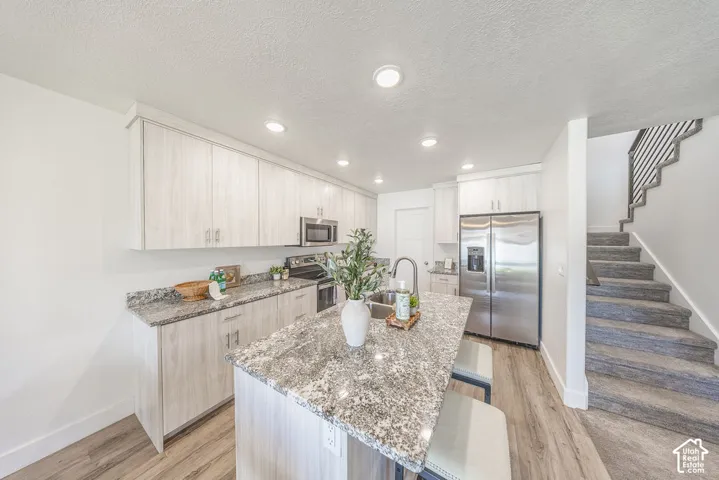 Modern kitchen featuring light wood-finish cabinetry, stainless steel appliances, granite-style countertops, an island with seating, and LVP flooring