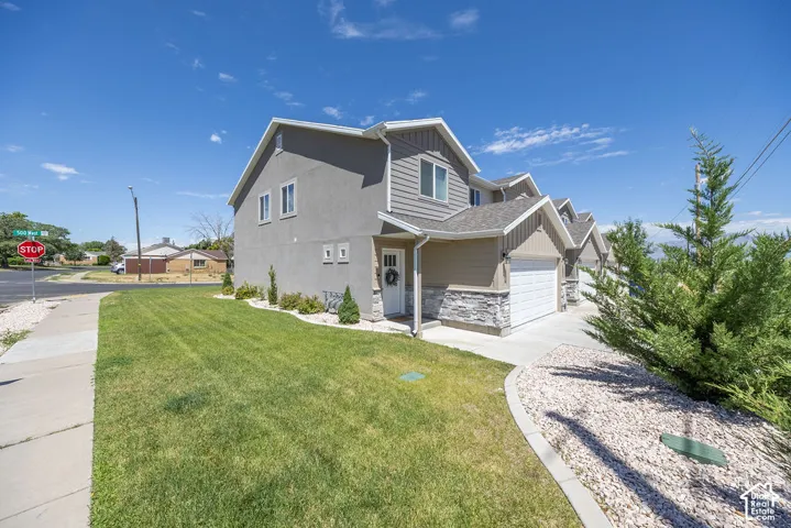 Multi-level property featuring a stucco and siding exterior, an attached garage, a manicured lawn, and a decorative stone landscaping bed!!!