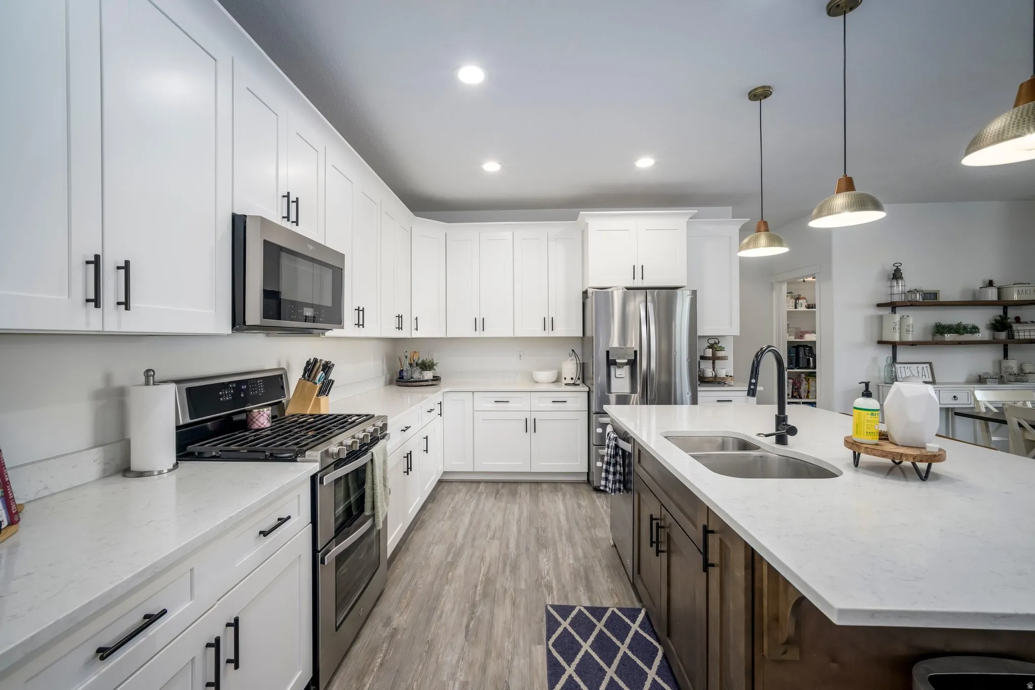 Modern kitchen featuring white cabinetry, stainless steel appliances, wood-finish flooring, a large island with a double basin sink, and recessed lighting
