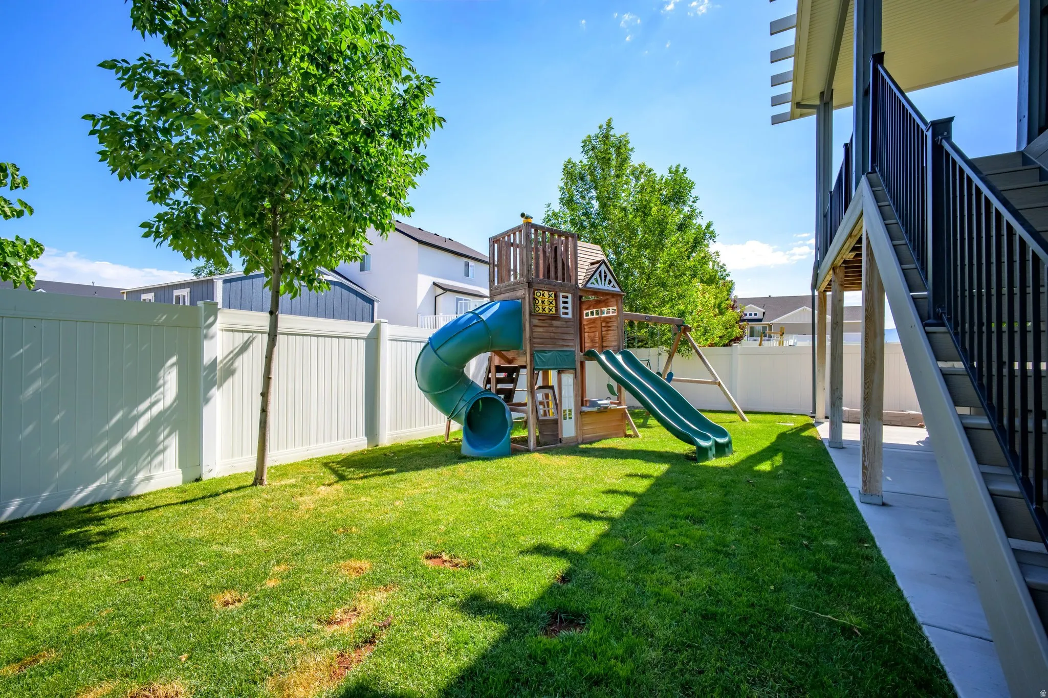 Expansive backyard featuring a manicured lawn, established trees, and a white privacy fence