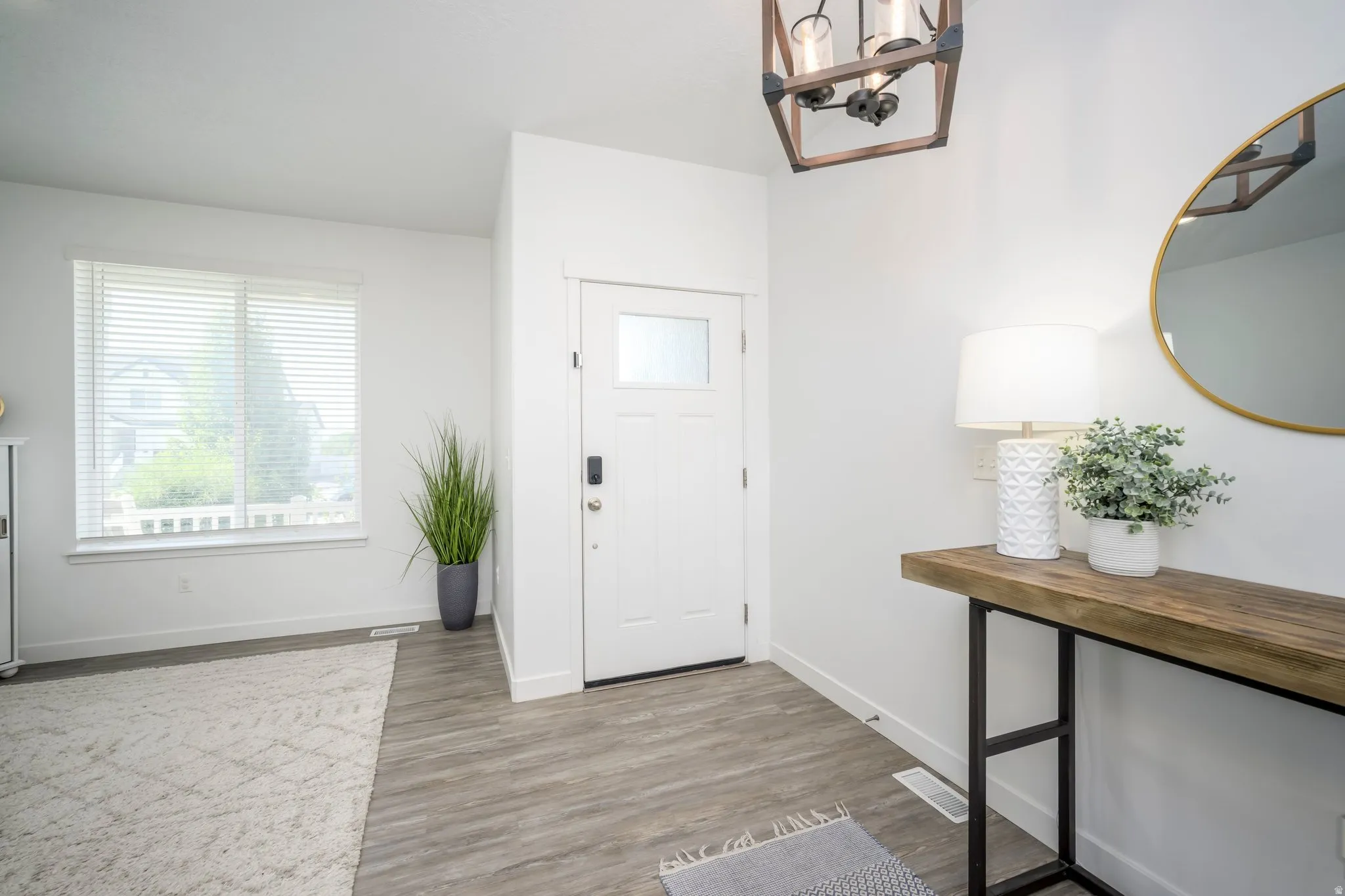 Entryway featuring wood-finish flooring, a white paneled door with frosted glass, and a modern rectangular chandelier
