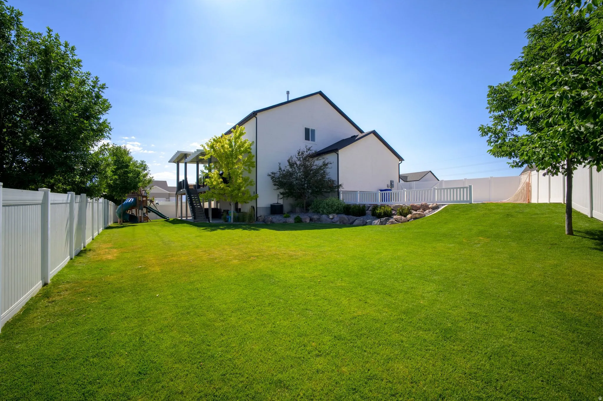 Expansive green lawn with mature trees and a white vinyl privacy fence