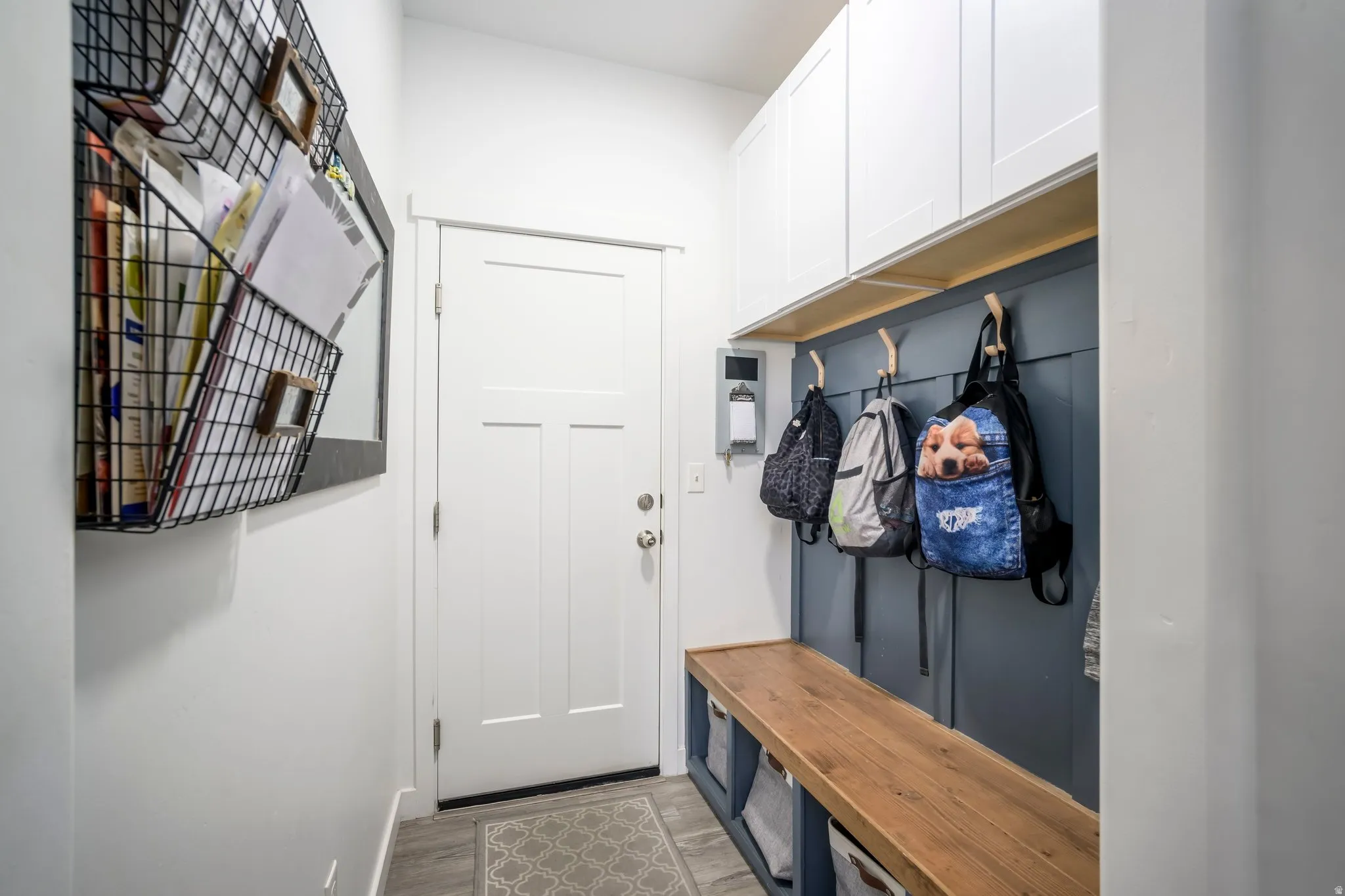 Entryway with built-in storage featuring an integrated wood-finish bench, upper white cabinetry, and wall-mounted hooks