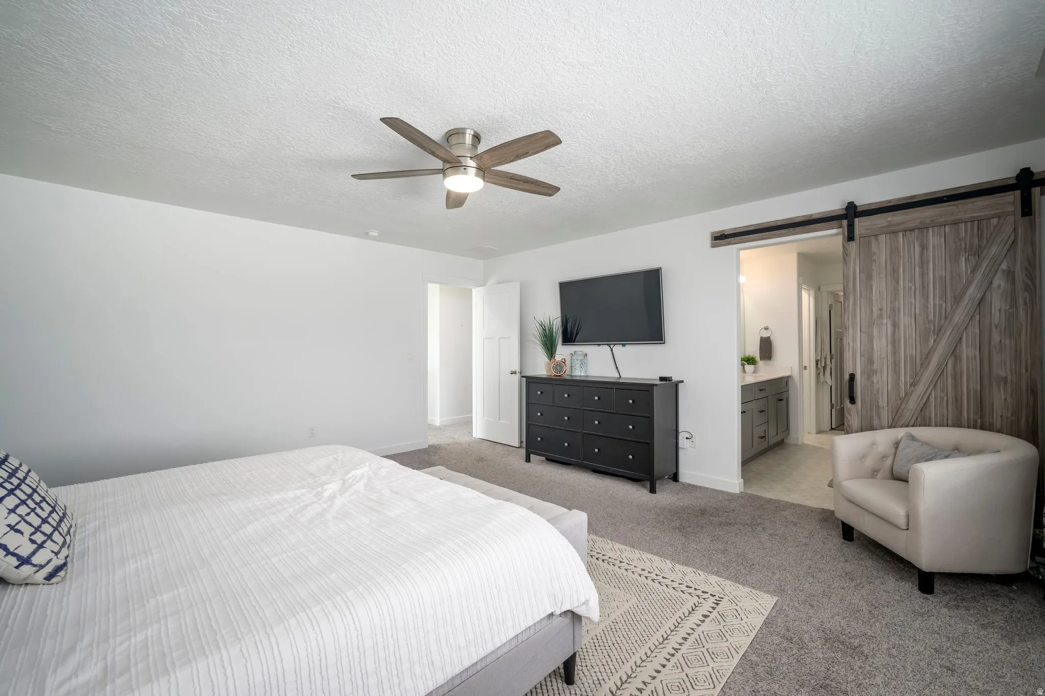 Spacious room featuring neutral carpeting, a ceiling fan, and a rustic wood-finish barn door