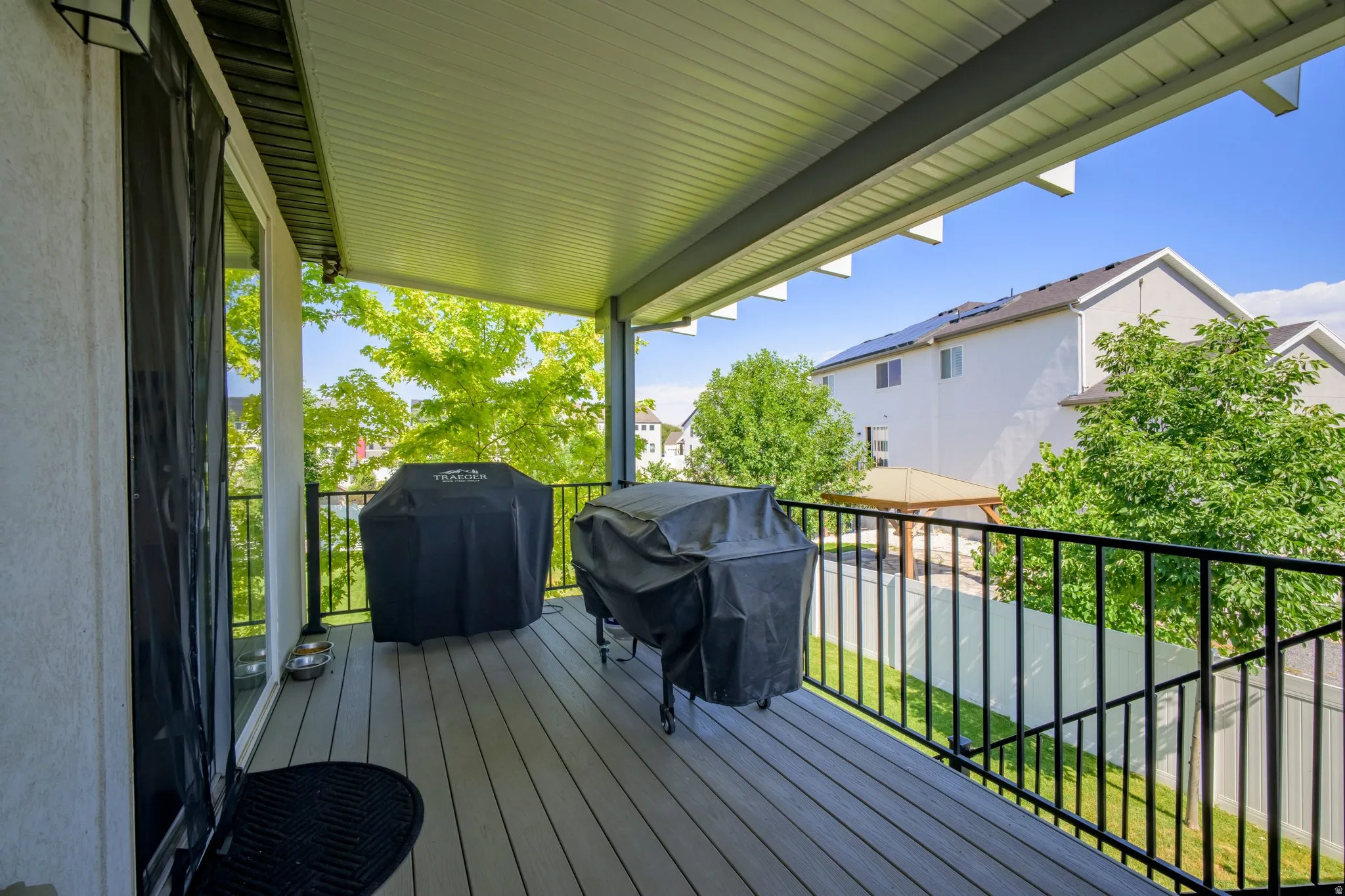 Covered outdoor deck with composite decking, black metal railings, and an exterior light fixture