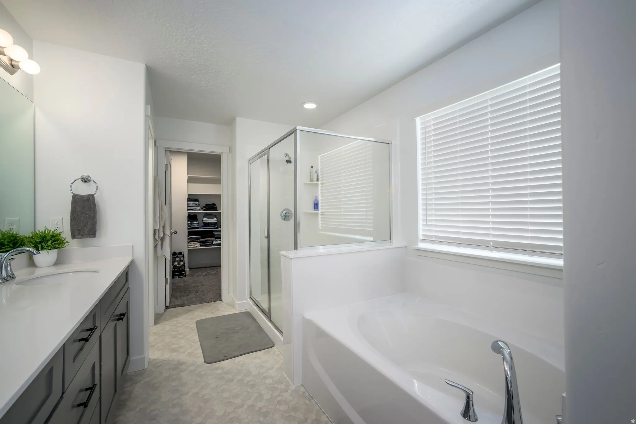 Modern bathroom featuring a soaking tub, glass-enclosed shower, single vanity with a white countertop, and light-toned flooring
