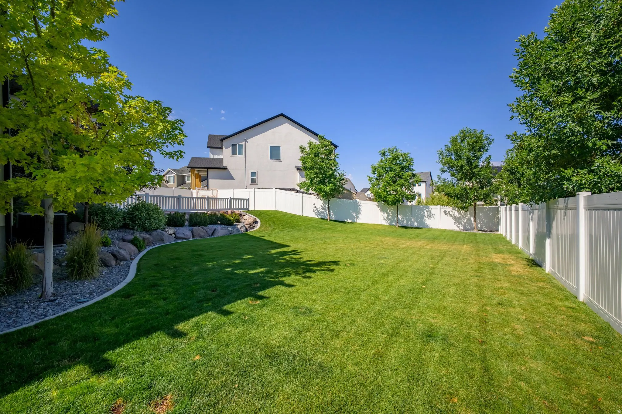 Spacious backyard featuring a manicured lawn, a large deck with railings, and a white privacy fence