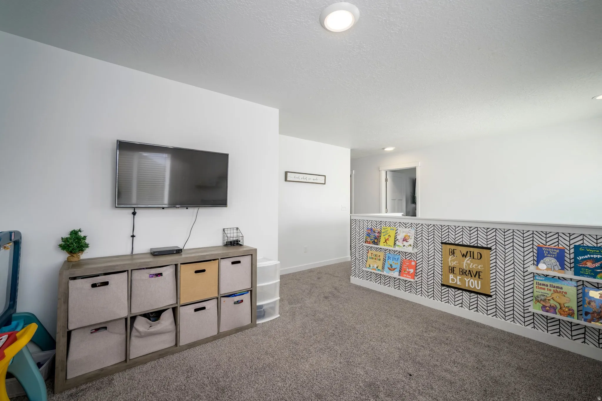 Loft area featuring neutral carpet flooring, white walls, and a decorative half-wall with shelving
