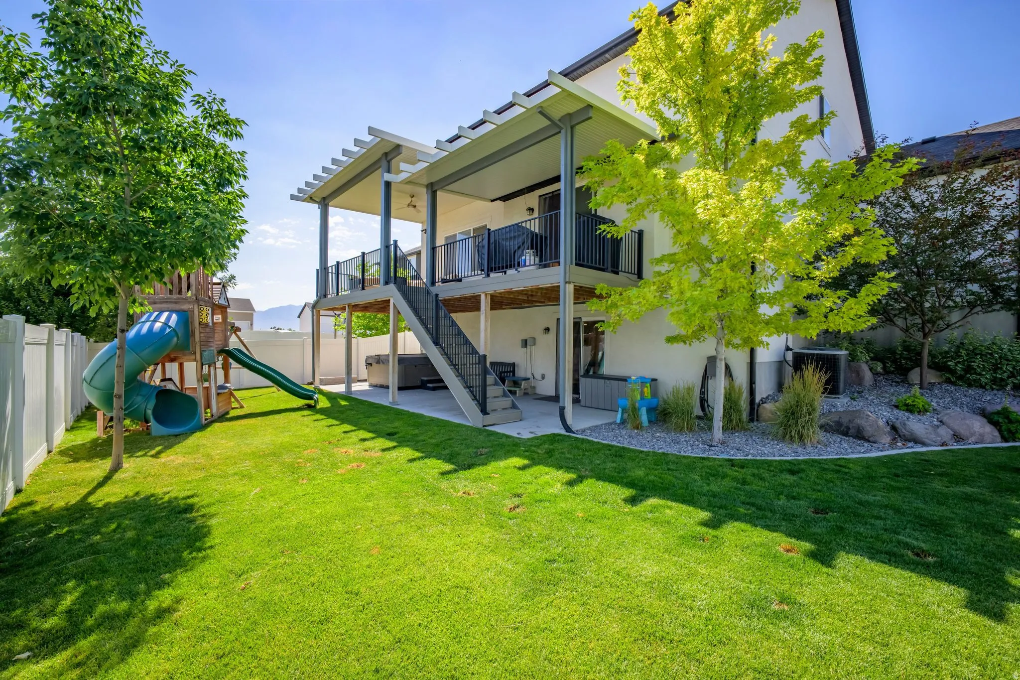 Expansive rear yard featuring a manicured lawn, a two-story covered deck with metal railings, and a lower patio area
