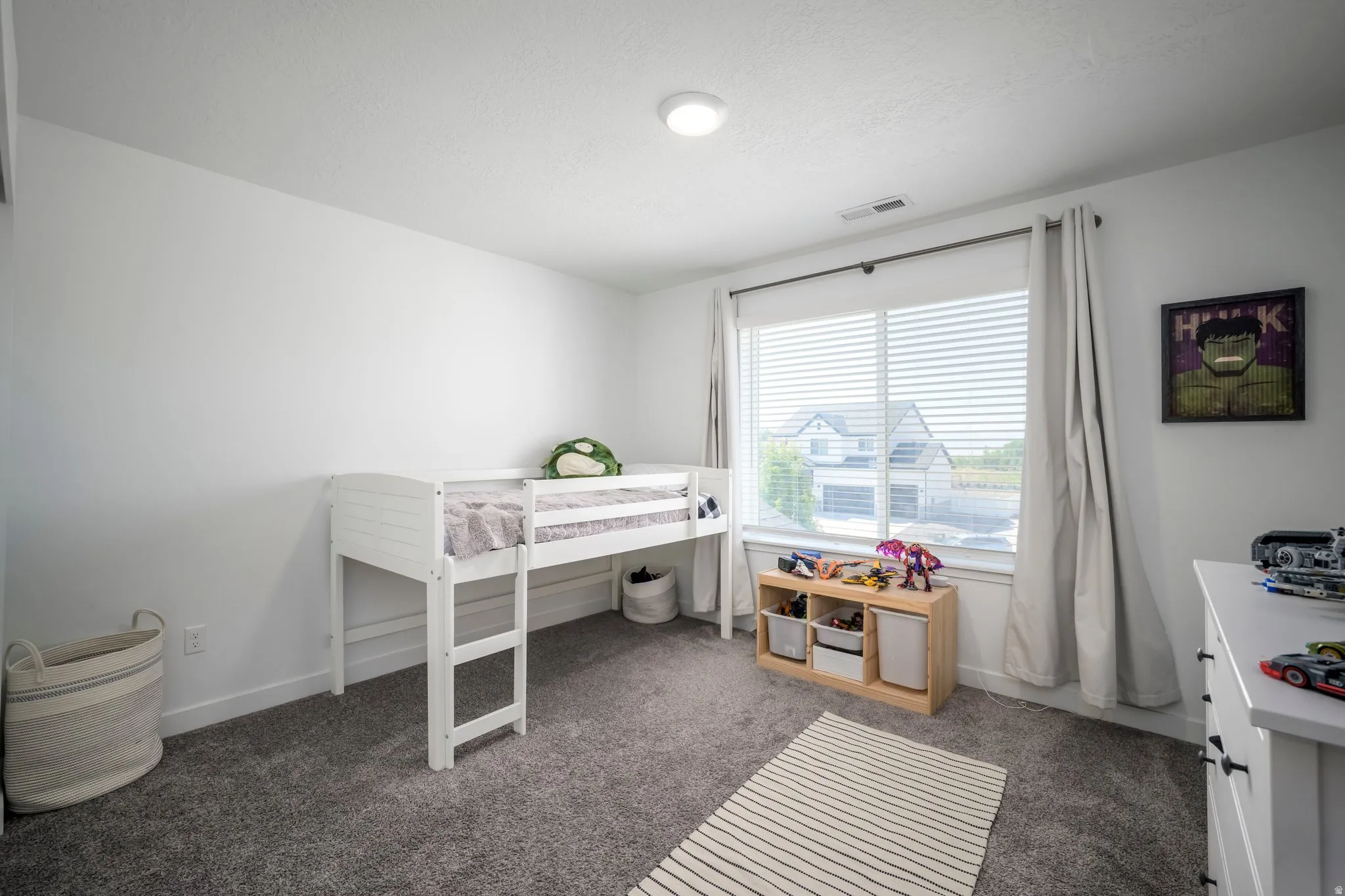 Bright room featuring a large window with horizontal blinds, neutral wall paint, and gray carpet flooring