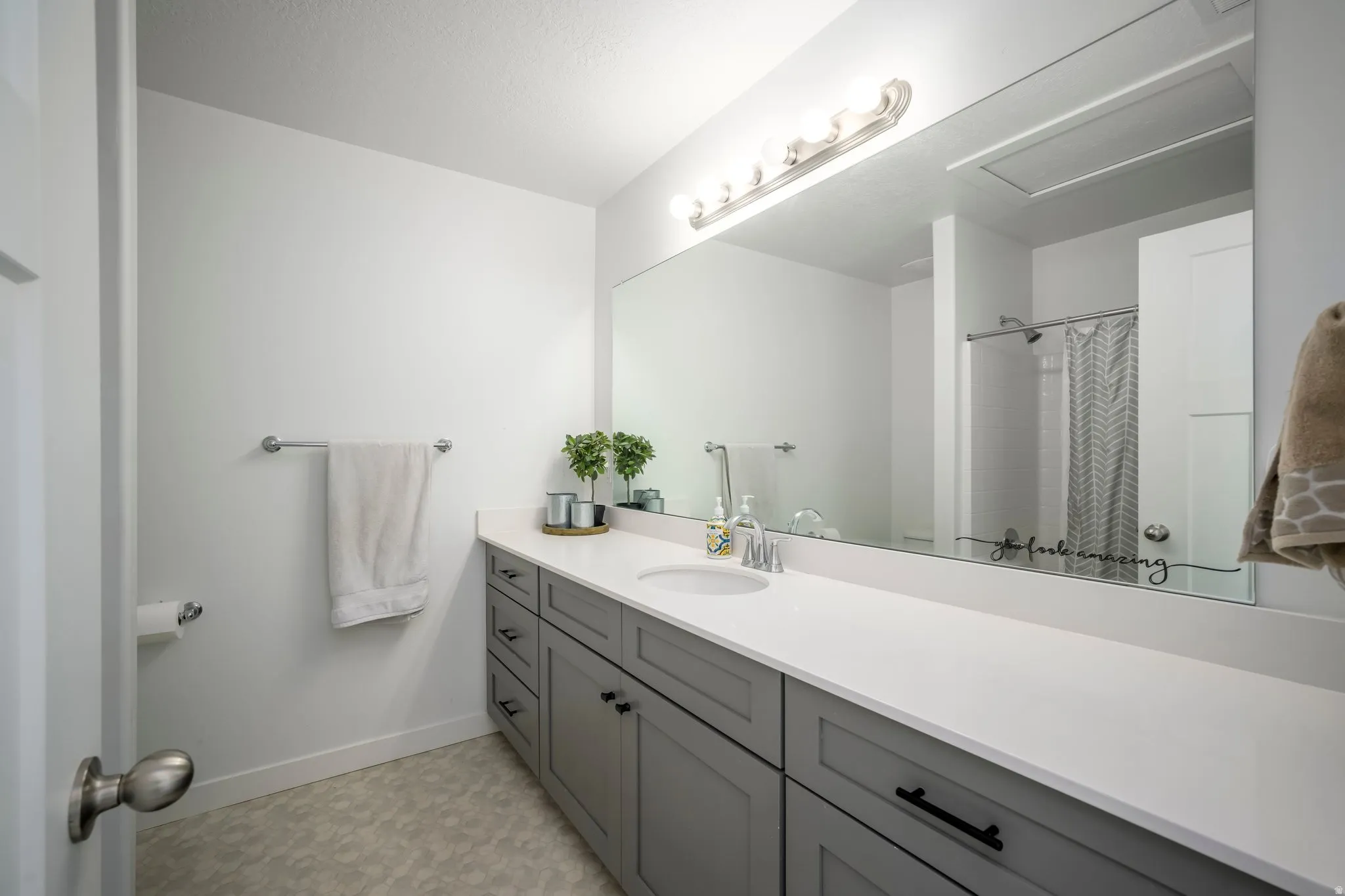 White bathroom featuring an elongated vanity with gray shaker-style cabinetry, a white countertop, and a single undermount sink