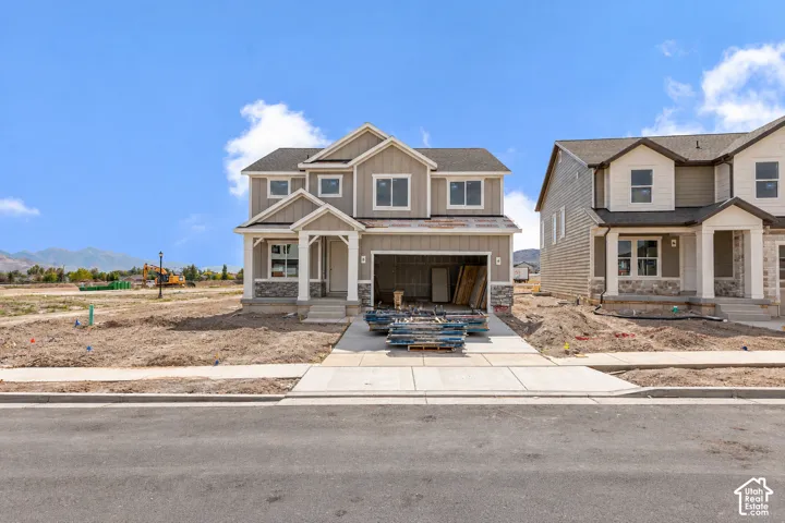 Two-story residence featuring a covered front porch, stone and siding exterior, two-car garage, and concrete driveway