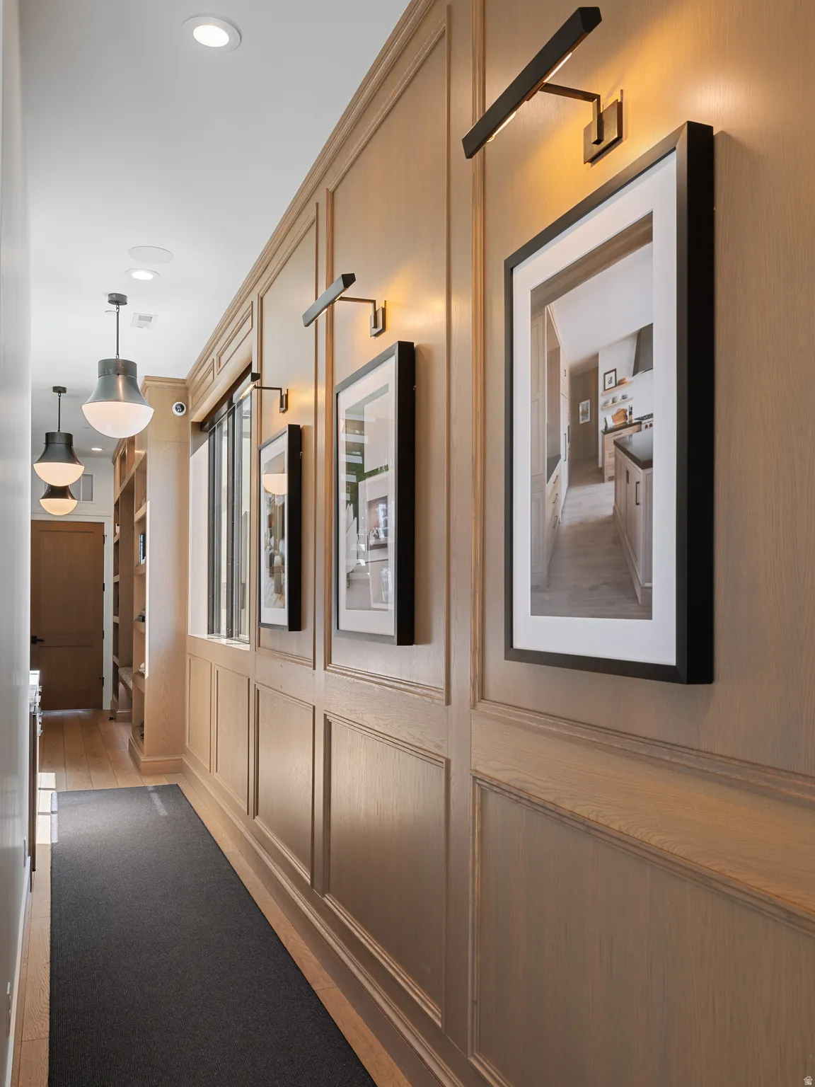 Hallway featuring paneled wood-finish walls, recessed lighting, accent picture lights, pendant lighting, and wood-finish flooring