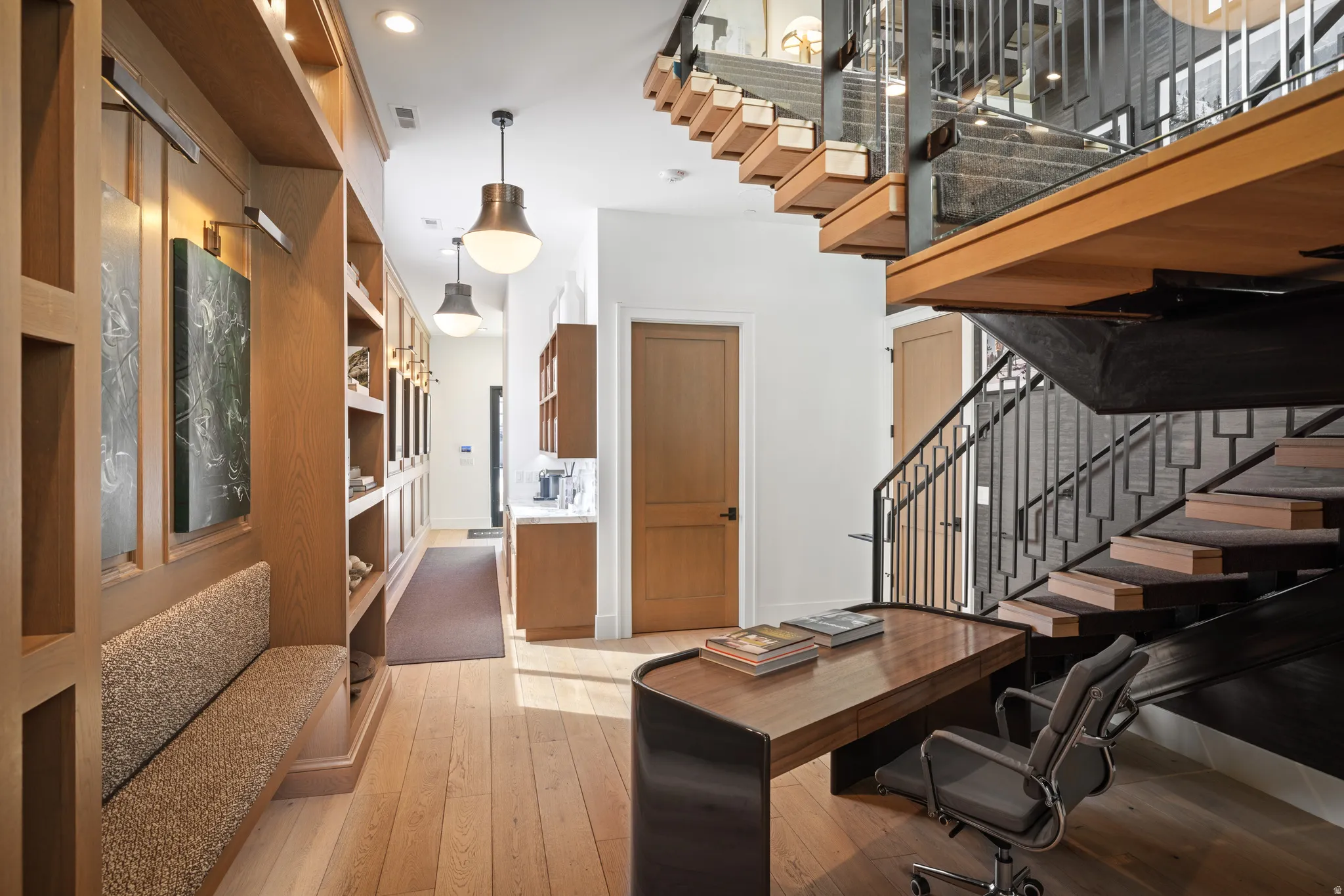 Open-concept interior featuring light wood-finish flooring, a built-in bench, and a floating staircase with dark metal railings